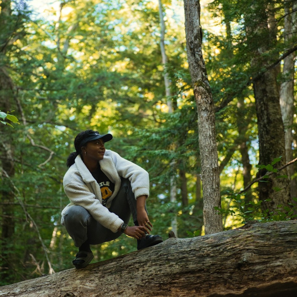 A woman pausing on a fallen log on a forest trail